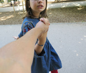 Cropped image of parent holding daughter hand on road