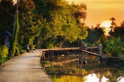 Footbridge over lake against sky during sunset