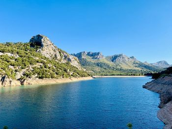 Scenic view of lake and mountains against clear blue sky