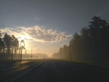 Empty road by trees against sky during sunset