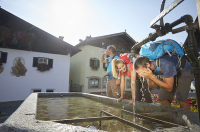 Hiker washing face by friends at fountain in village on sunny day, mutters, tyrol, austria