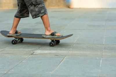 Low section of man skateboarding on skateboard with sandals