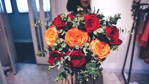 Woman holding bunch of roses while standing at home