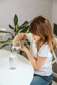 A cute little girl pours pure mineral water from a bottle into a glass. thirst. 