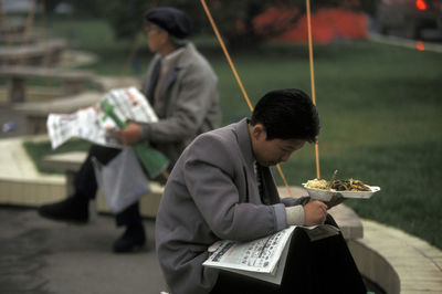 Businessman reading newspaper while holding food plate