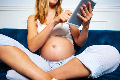 Midsection of woman using mobile phone while sitting on bed at home