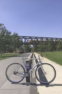 Bicycle parked by railing against clear blue sky