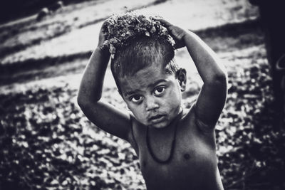 Portrait of shirtless boy carrying flowers on head outdoors