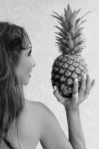 Rear view of shirtless woman holding pineapple against wall