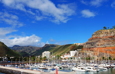 Sailboats moored at harbor by mountains against blue sky