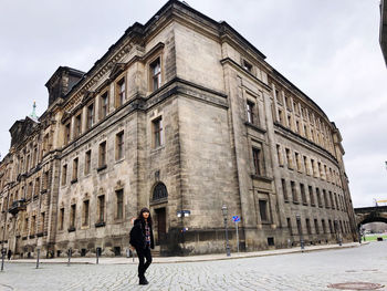 Woman walking on street amidst buildings in city against sky