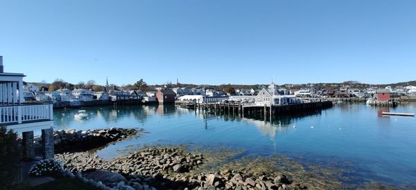 Sailboats in harbor by buildings against clear blue sky