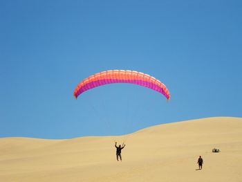 Man paragliding in desert against clear blue sky