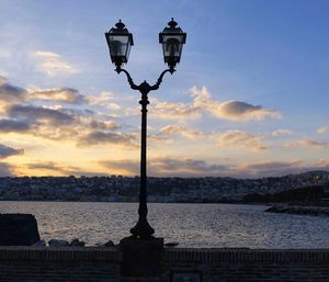 Street light by sea against sky during sunset