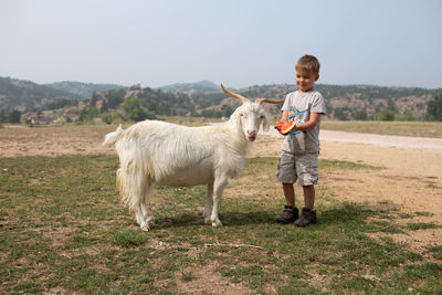 Boy feeding goat watermelon with mountains in background