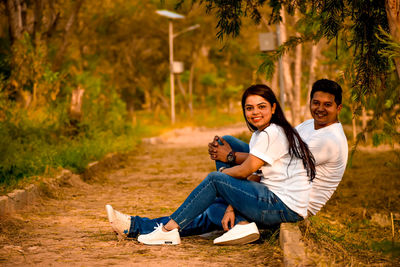 Portrait of young couple sitting on plants against trees