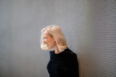 Side view of smiling woman standing by wall