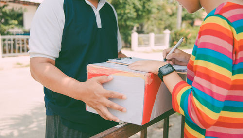 Midsection of woman signing document while receiving parcel outdoors