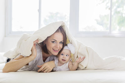 Portrait of mother and daughter lying on bed under blanket