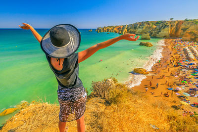 Rear view of woman standing on cliff against sea