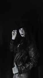 Portrait of young woman standing against black background