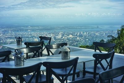 Chairs and tables on table by buildings in city against sky