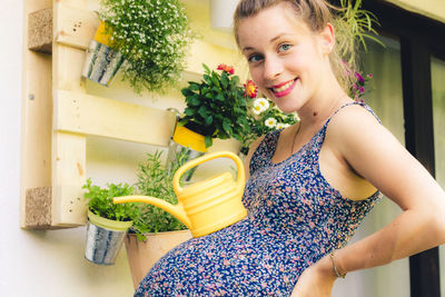 Beautiful pregnant young woman watering plants on her balcony