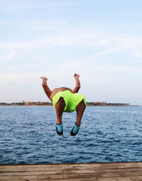 Man jumping from pier in sea against clear sky