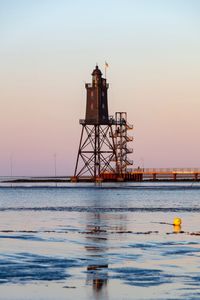 Lighthouse by sea against sky during sunset