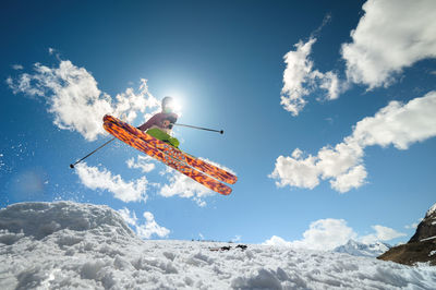 A woman skier makes a jump trick, covering the sun. flying skier against the background
