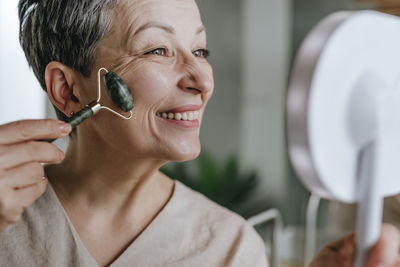 Happy woman using jade roller on face at home