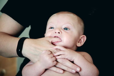 Baby sucking his father thumb while sitting at home