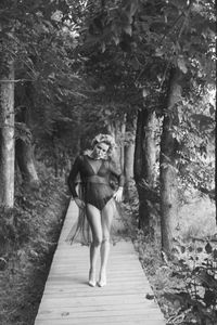 Portrait of woman with hands on hip standing on footpath at forest