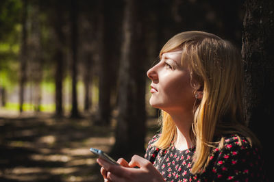 Woman using mobile phone by tree trunk in forest