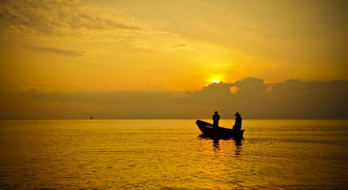 Silhouette people in sea against sky during sunset