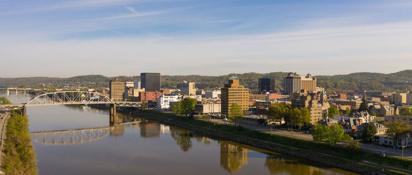 Bridge over river amidst buildings in city against sky