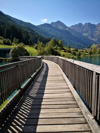 Footbridge leading towards mountains against sky