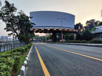 Road by plants and city against sky