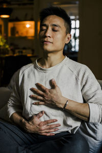 Man with hands on chest meditating at home