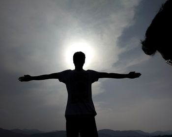 Silhouette man with arms outstretched standing against sky during sunset