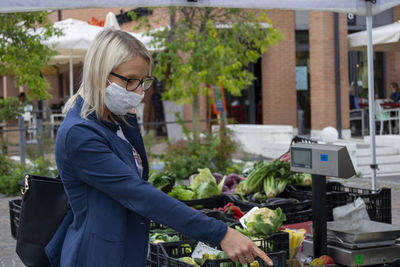 Women with mask at farmer's market, buying vegetables.