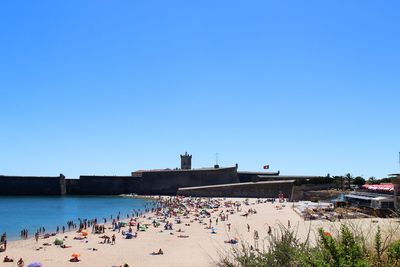 People at beach against clear blue sky