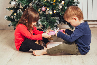 Side view of siblings sitting on hardwood floor