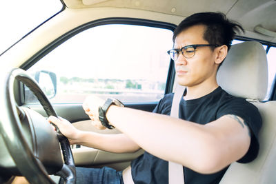 Man wearing eyeglasses checking time while sitting in car