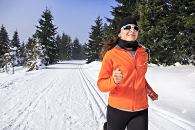 Woman running on snow covered field against sky
