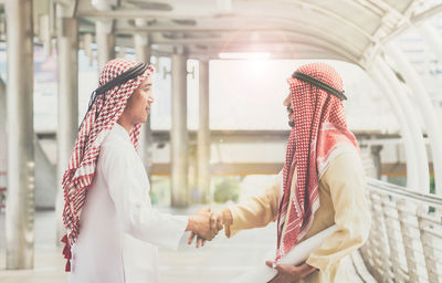 Side view of men in thobes shaking hands while standing on footbridge