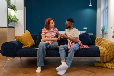 Unhappy young diverse married couple sitting on sofa talking about problems in relationship