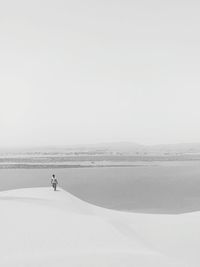 Mid distance view of man walking at desert with lake in background against clear sky