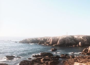 Scenic view of sea and rocks against clear sky