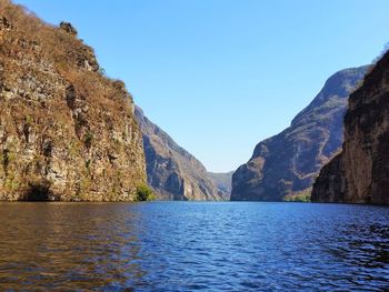 Scenic view of sea and mountains against clear blue sky
